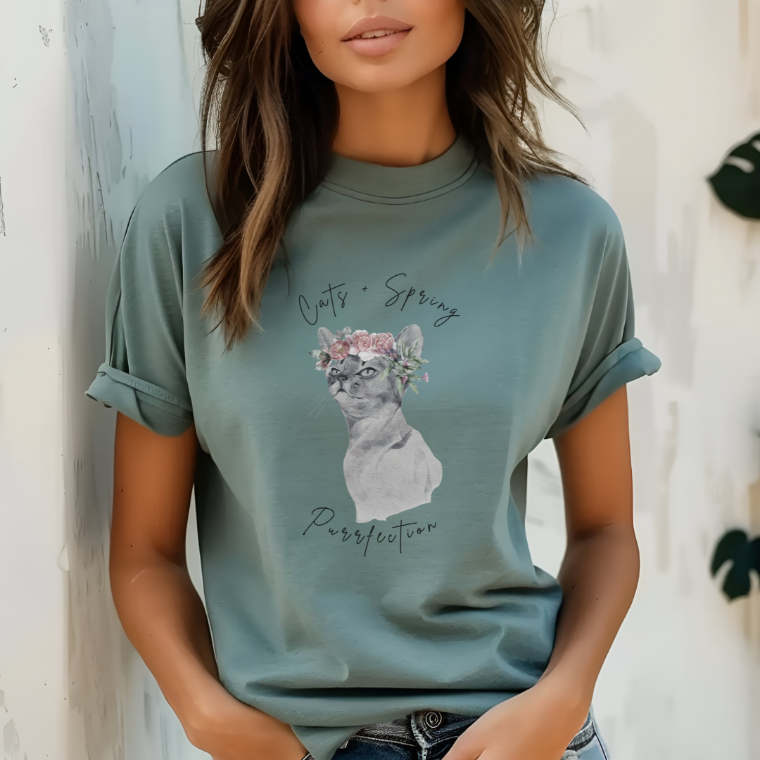 "Purrfect Spring Vibes" Personalized Unisex Garment-Dyed T-Shirt, featuring a charming watercolor illustration of a grey cat wearing a crown of pink roses and green leaves, with the text "Cats + Spring Purrfection" above and below, modeled by a woman wearing size L for an oversized effect. Color Light green