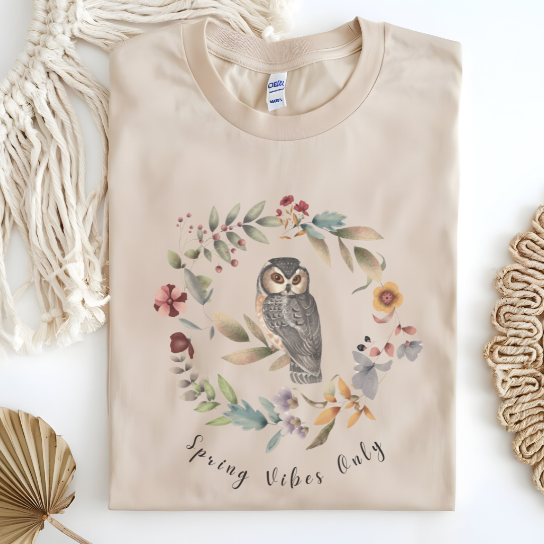 Flat lay of the "Spring Vibes Only" Tee, highlighting the soft, 100% US cotton fabric, classic crew neck, and the adorable owl and floral wreath design. Color Sand