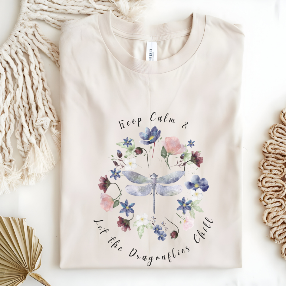 Flat lay of the "Chill Spring! Keep Calm & Let the Dragonflies Chill" T-Shirt, highlighting the soft, 100% ring-spun cotton fabric, classic crew neck, and the adorable dragonfly and floral wreath design. Color Natural