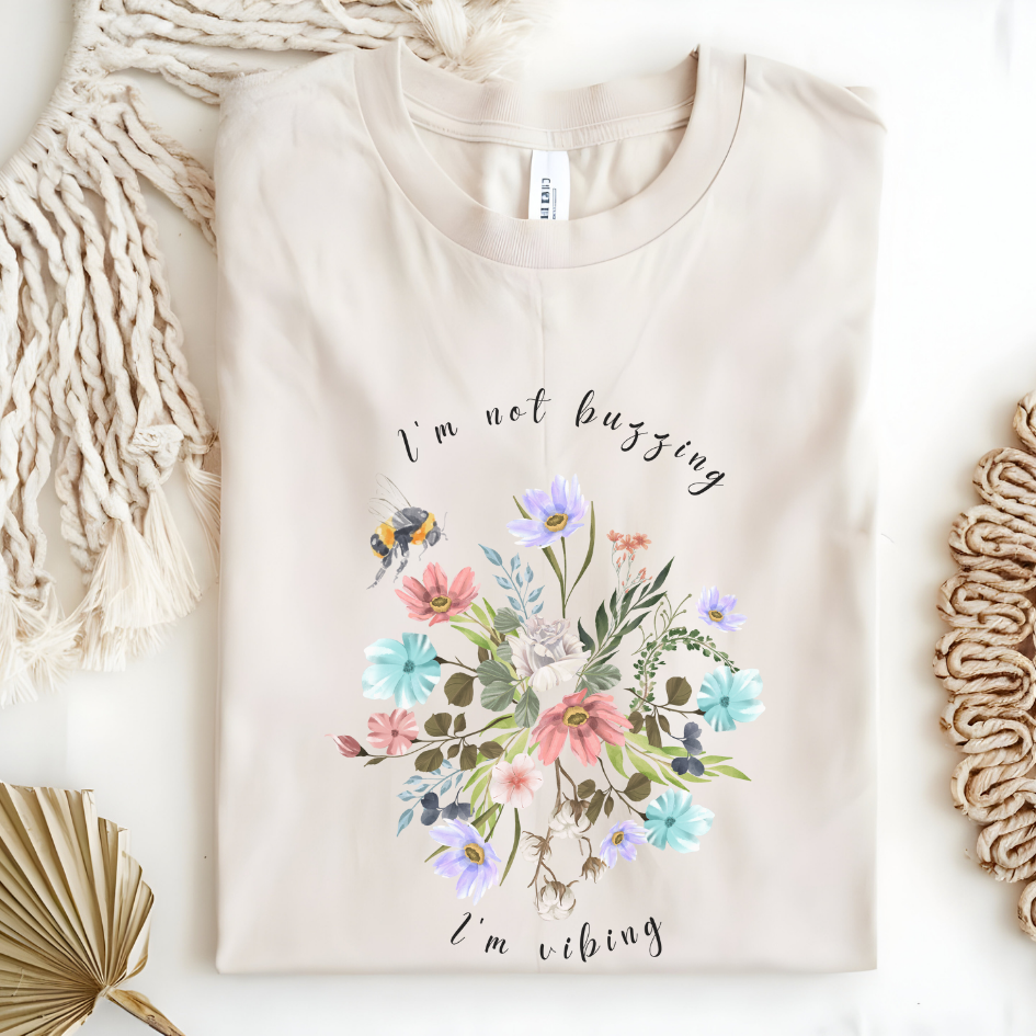 Flat lay of the "Sweet Spring! I'm Not Buzzing" T-Shirt, highlighting the soft, 100% ring-spun cotton fabric, classic crew neck, and the adorable bee and wildflower design. Color Natural
