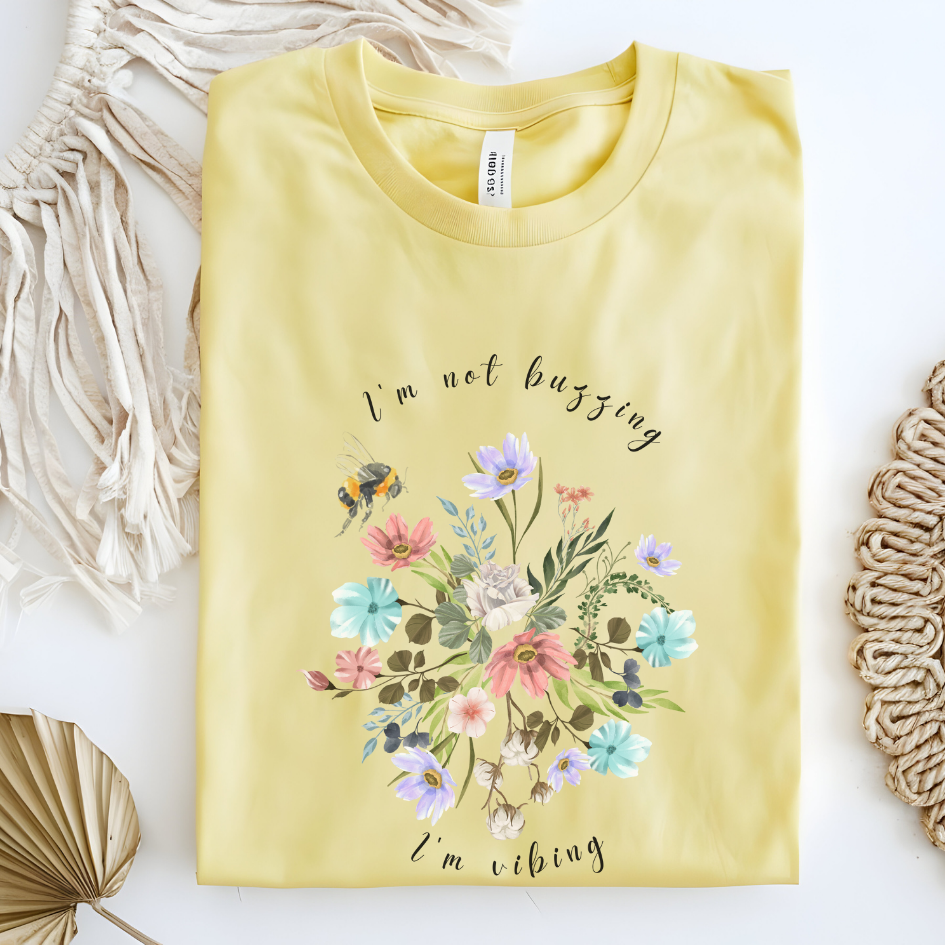 Flat lay of the "Sweet Spring! I'm Not Buzzing" T-Shirt, highlighting the soft, 100% ring-spun cotton fabric, classic crew neck, and the adorable bee and wildflower design. Color Cornsilk