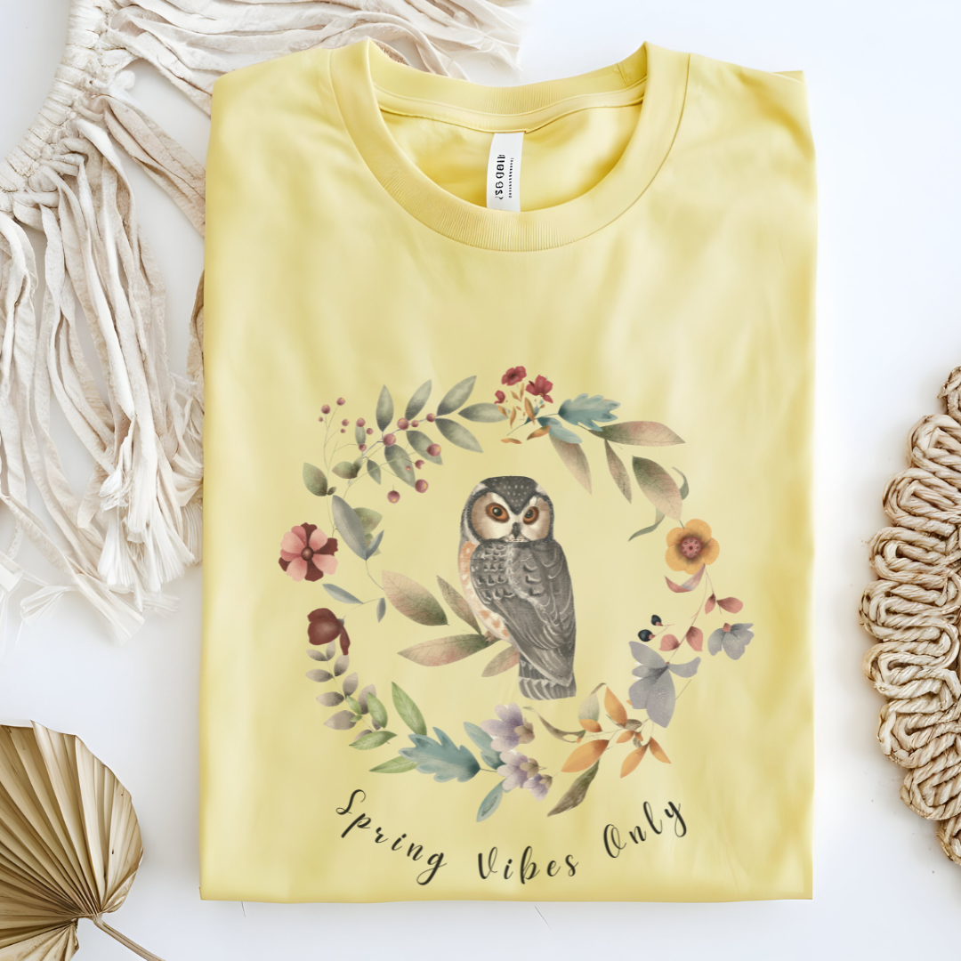 Flat lay of the "Spring Vibes Only" Tee, highlighting the soft, 100% US cotton fabric, classic crew neck, and the adorable owl and floral wreath design. Color Cornsilk