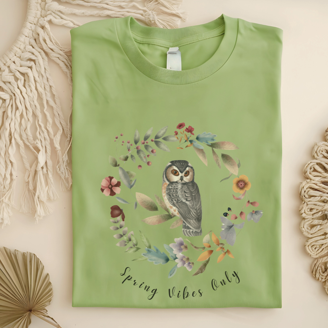 Flat lay of the "Spring Vibes Only" Tee, highlighting the soft, 100% US cotton fabric, classic crew neck, and the adorable owl and floral wreath design. Color Pistachio