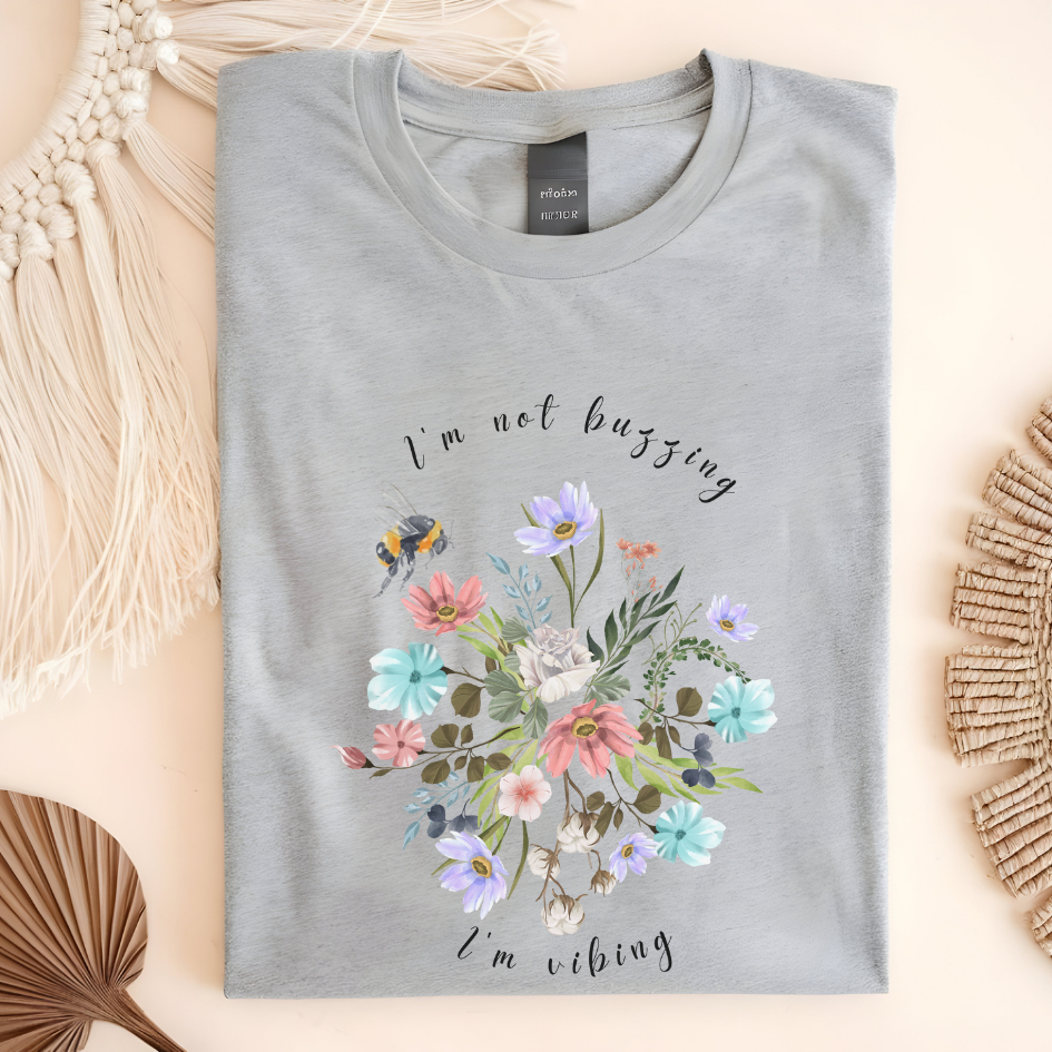 Flat lay of the "Sweet Spring! I'm Not Buzzing" T-Shirt, highlighting the soft, 100% ring-spun cotton fabric, classic crew neck, and the adorable bee and wildflower design. Color Sport grey