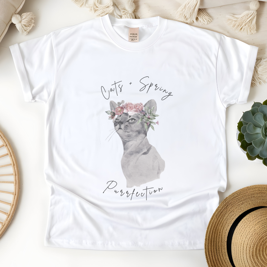 Flat lay of the "Purrfect Spring Vibes" T-Shirt, highlighting the garment-dyed fabric's texture and the durable double-needle stitching. The watercolor cat and floral crown design. Color IWhite