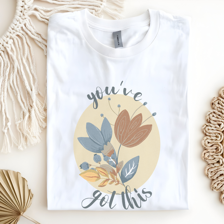 Cotton unisex t-shirt with "you've got this" motivational text and artistic floral design in blue, terracotta, and cream colors. White