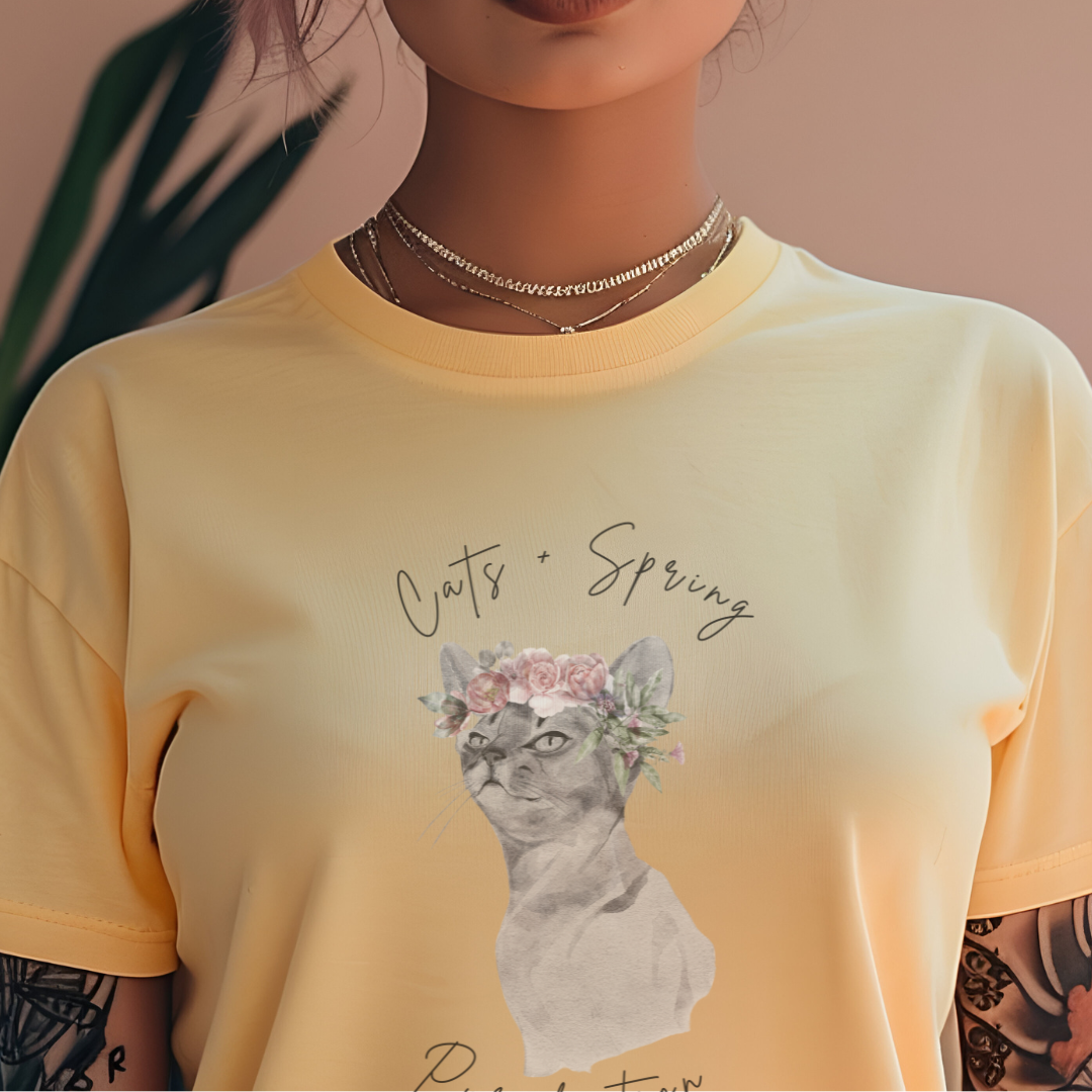 "Purrfect Spring Vibes" Personalized Unisex Garment-Dyed T-Shirt, featuring a charming watercolor illustration of a grey cat wearing a crown of pink roses and green leaves, with the text "Cats + Spring Purrfection" above and below, modeled by a woman wearing size L for an oversized effect. Color Banana