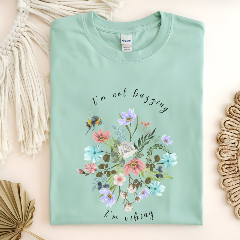 Flat lay of the "Sweet Spring! I'm Not Buzzing" T-Shirt, highlighting the soft, 100% ring-spun cotton fabric, classic crew neck, and the adorable bee and wildflower design. Color Mint green