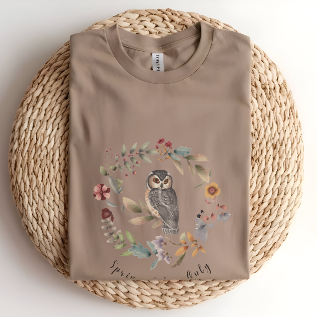 Flat lay of the "Spring Vibes Only" Tee, highlighting the soft, 100% US cotton fabric, classic crew neck, and the adorable owl and floral wreath design. Color Tan