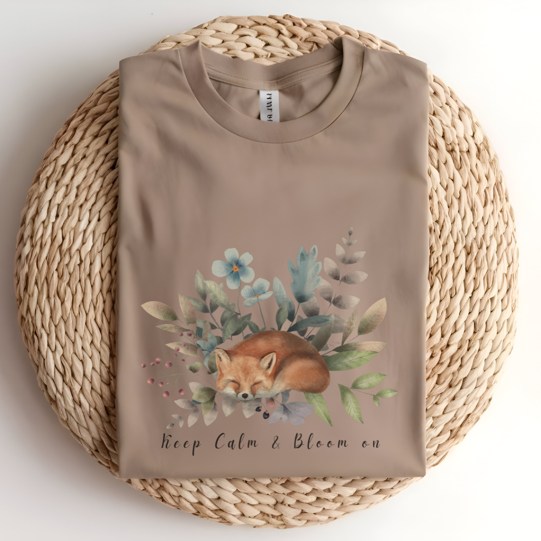 Flat lay of the "Keep Calm & Bloom On" T-Shirt, highlighting the soft, 100% US cotton fabric and classic crew neck. The watercolor fox and floral design are clearly visible. Color Tan