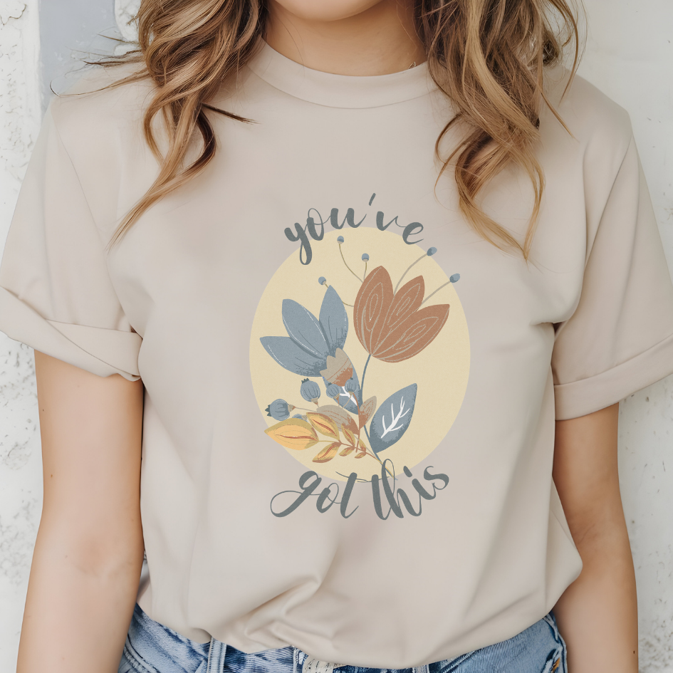 Cotton unisex t-shirt with "you've got this" motivational text and artistic floral design in blue, terracotta, and cream colors. Color sand