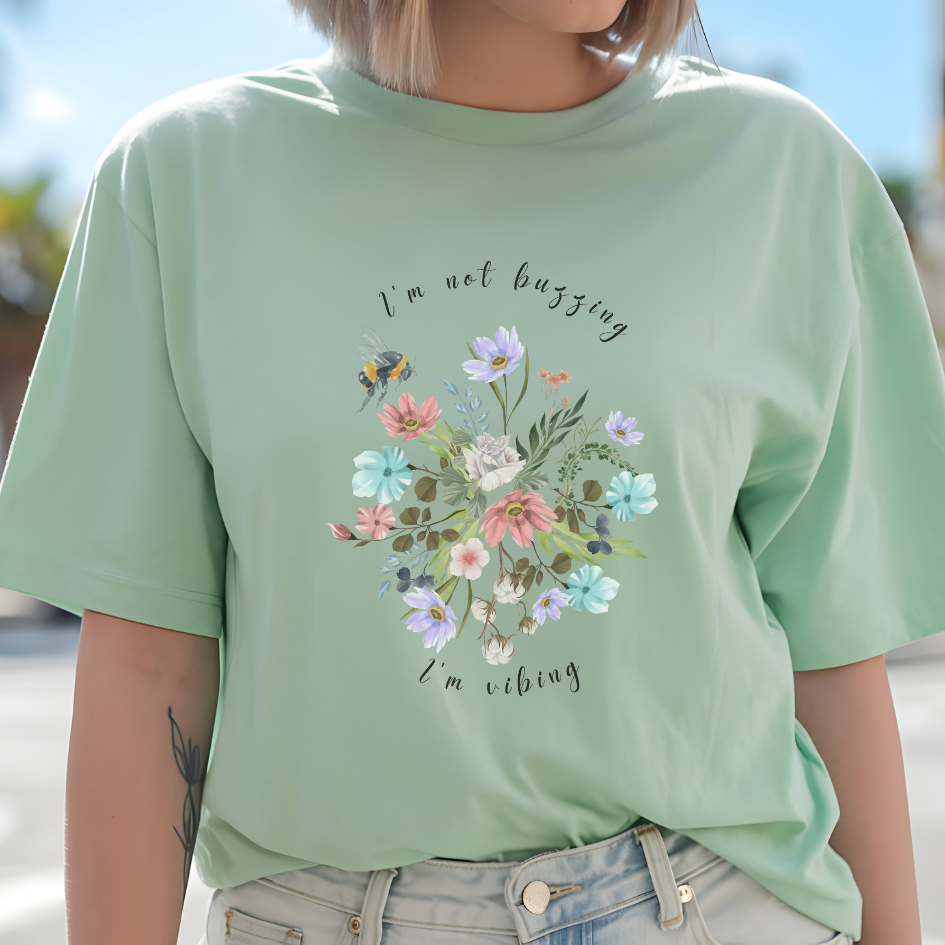 Close-up view of the "I'm Not Buzzing" graphic, showcasing the detailed illustration of the bee with its delicate wings and fuzzy body, the intricate details of the wildflower petals and leaves, and the whimsical typography of the "I'm Not Buzzing" and "I'm Vibing" text.