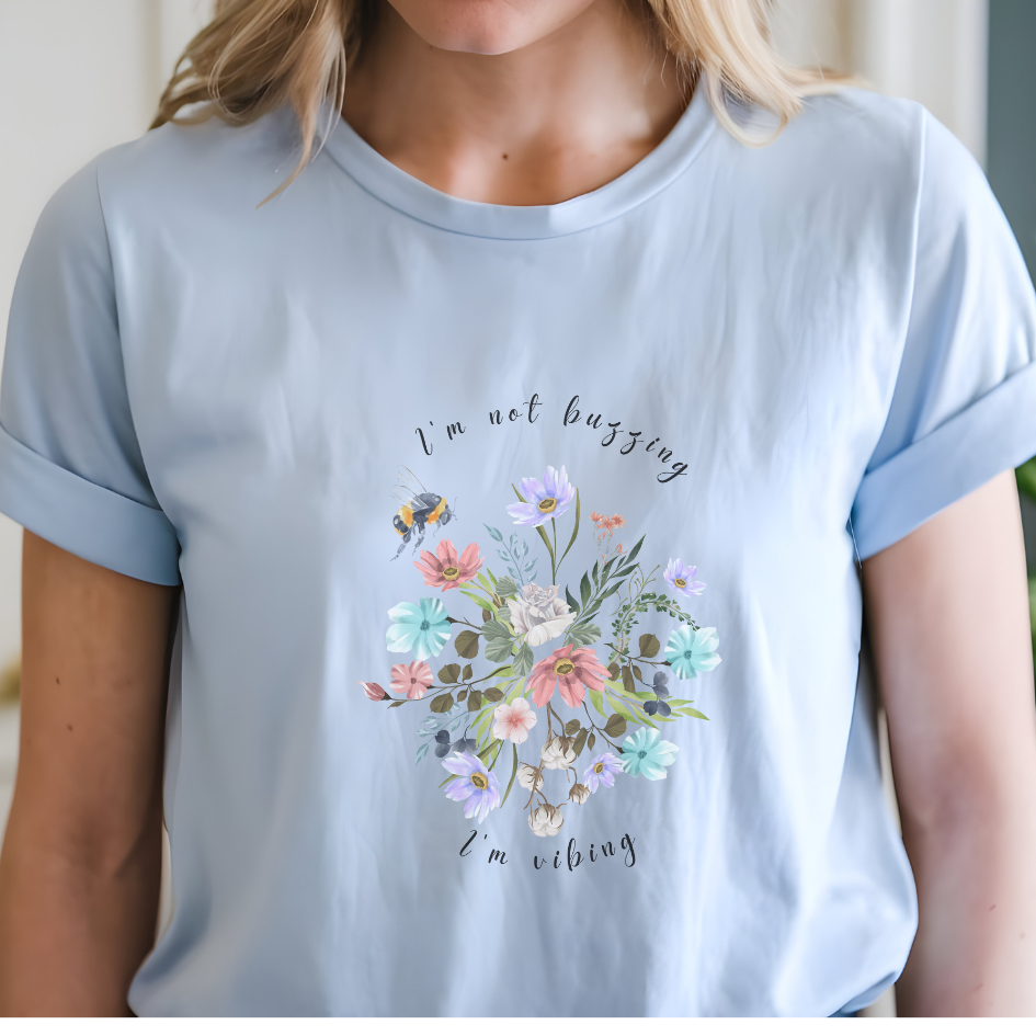 Close-up view of the "I'm Not Buzzing" graphic, showcasing the detailed illustration of the bee with its delicate wings and fuzzy body, the intricate details of the wildflower petals and leaves, and the whimsical typography of the "I'm Not Buzzing" and "I'm Vibing" text. Color Light blue