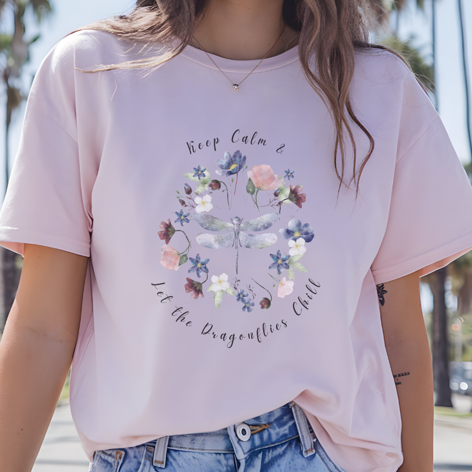 Close-up view of the "Keep Calm & Let the Dragonflies Chill" graphic, showcasing the detailed illustration of the dragonfly with its intricate wings and delicate body, the vibrant colors and textures of the wildflower petals and leaves in the wreath, and the calming typography of the "Keep Calm & Let the Dragonflies Chill" text. Color Light Pink