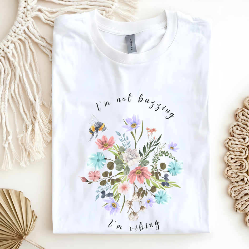 Flat lay of the "Sweet Spring! I'm Not Buzzing" T-Shirt, highlighting the soft, 100% ring-spun cotton fabric, classic crew neck, and the adorable bee and wildflower design. Color white