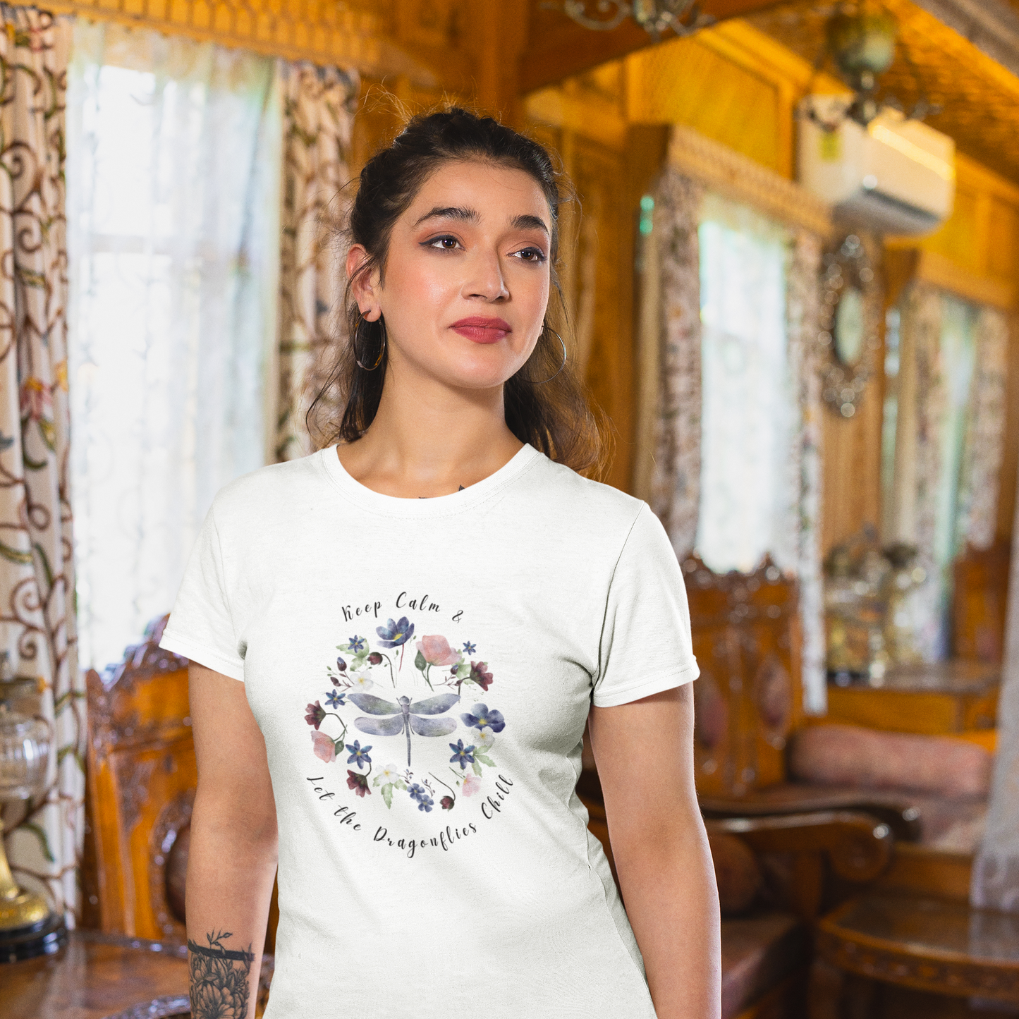Chill Spring! Keep Calm & Let the Dragonflies Chill" Unisex Soft Style T-Shirt, featuring a charming illustration of a delicate dragonfly at the center of a circular wreath of blooming wildflowers, with the text "Keep Calm & Let the Dragonflies Chill" elegantly encircling the design, modeled by a eoman wearing size S. Color White