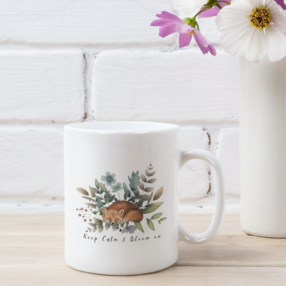 Keep Calm & Bloom On Ceramic Mug featuring a circular design of vibrant wildflowers and a sleeping fox, on a white background. Available in 11oz and 15oz sizes.