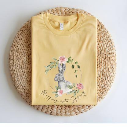 Flat lay of the "Hoppin' into Spring" T-Shirt, highlighting the garment-dyed fabric's texture and the durable double-needle stitching. The watercolor bunny and floral wreath design are clearly visible. Color Butter