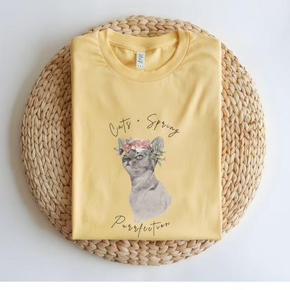 Flat lay of the "Purrfect Spring Vibes" T-Shirt, highlighting the garment-dyed fabric's texture and the durable double-needle stitching. The watercolor cat and floral crown design. Color Butter