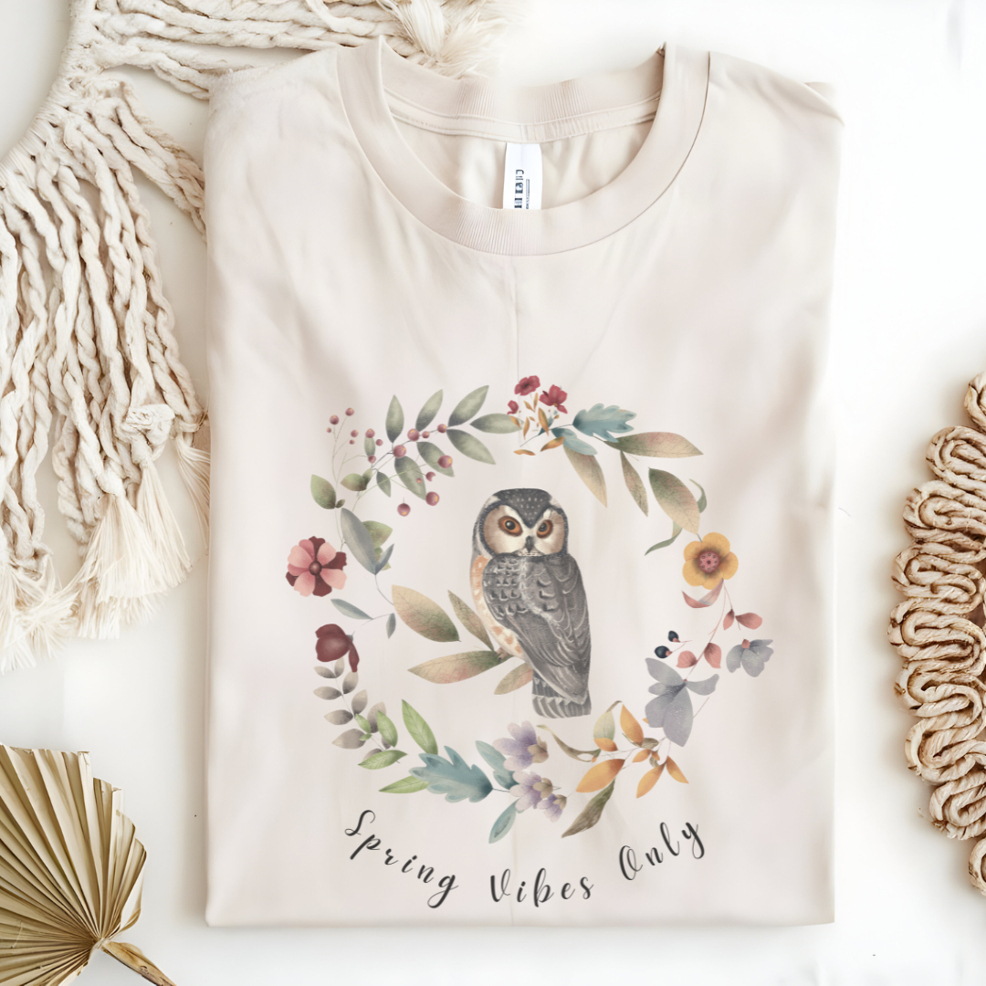 Flat lay of the "Spring Vibes Only" Tee, highlighting the soft, 100% US cotton fabric, classic crew neck, and the adorable owl and floral wreath design.  Color Natural
