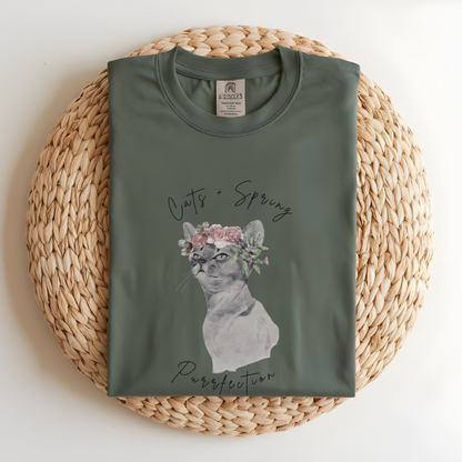 Flat lay of the "Purrfect Spring Vibes" T-Shirt, highlighting the garment-dyed fabric's texture and the durable double-needle stitching. The watercolor cat and floral crown design. Light green