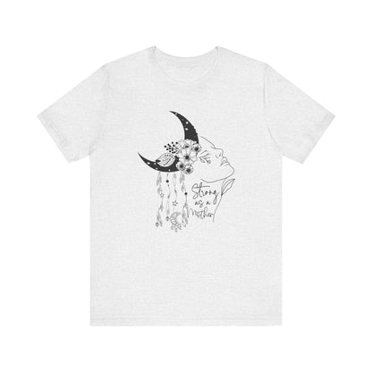 Flat lay of the "Strong as a Mother" T-Shirt, highlighting the soft Airlume cotton fabric and classic crew neckline. Color Ash. The graphic is clearly visible, showing the woman's profile, crescent moon, flowers, and charms in detail.