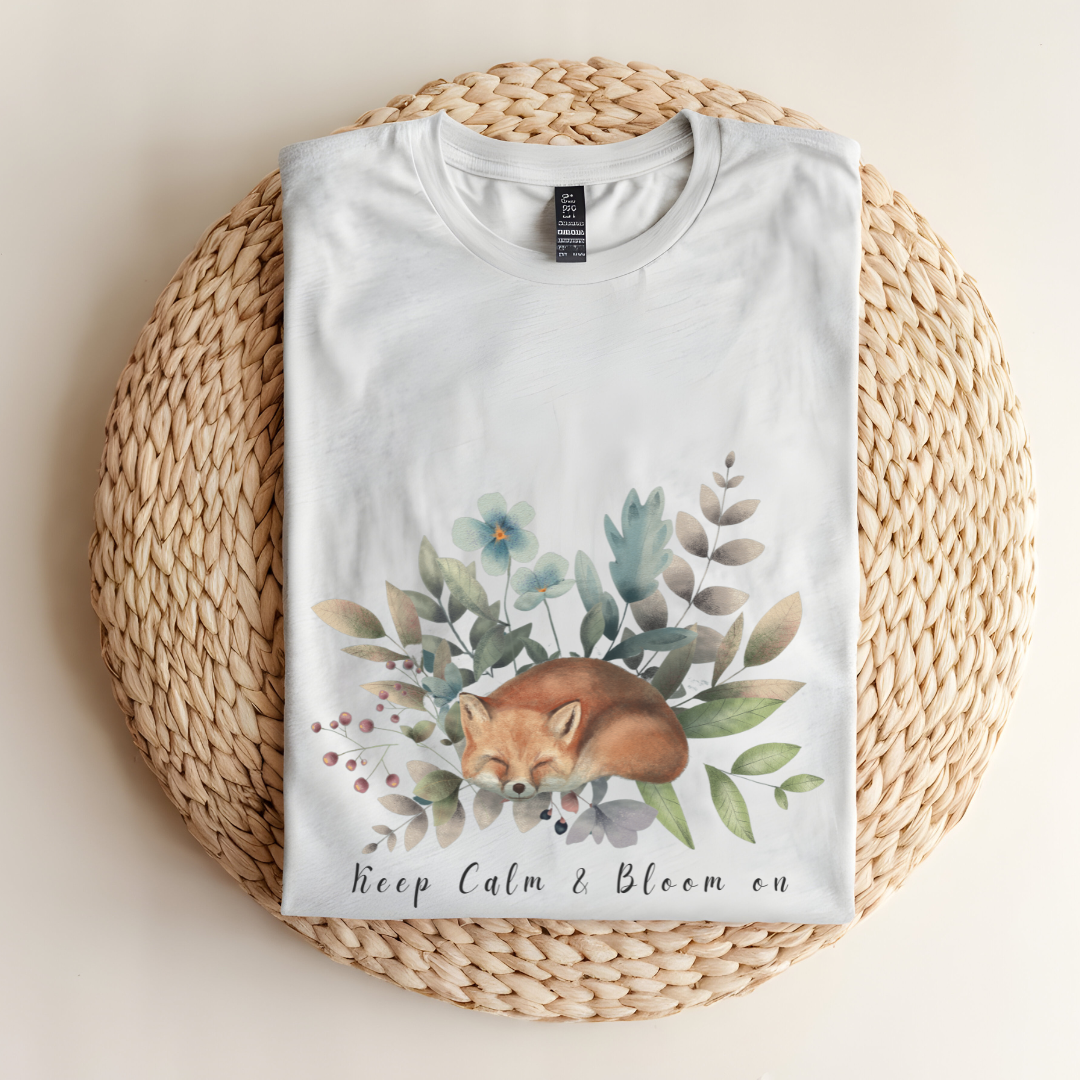 Flat lay of the "Keep Calm & Bloom On" T-Shirt, highlighting the soft, 100% US cotton fabric and classic crew neck. The watercolor fox and floral design are clearly visible. Color Ash