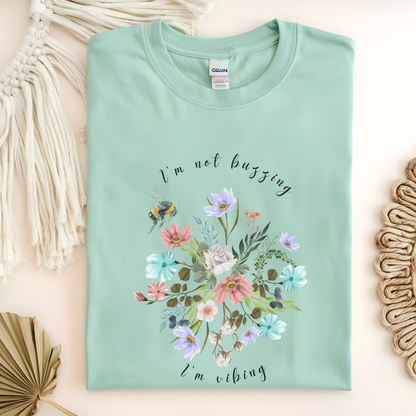 Flat lay of the "Sweet Spring! I'm Not Buzzing" T-Shirt, highlighting the soft, 100% ring-spun cotton fabric, classic crew neck, and the adorable bee and wildflower design. Color Mint green