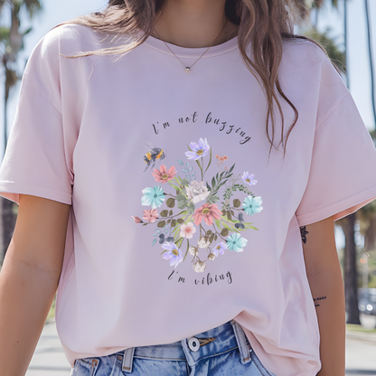 Close-up view of the "I'm Not Buzzing" graphic, showcasing the detailed illustration of the bee with its delicate wings and fuzzy body, the intricate details of the wildflower petals and leaves, and the whimsical typography of the "I'm Not Buzzing" and "I'm Vibing" text. Color Light pink