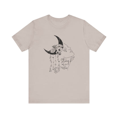 Flat lay of the "Strong as a Mother" T-Shirt, highlighting the soft Airlume cotton fabric and classic crew neckline. Color Heather Clay Gray. The graphic is clearly visible, showing the woman's profile, crescent moon, flowers, and charms in detail.