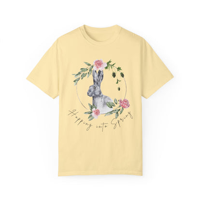 Flat lay of the "Hoppin' into Spring" T-Shirt, highlighting the garment-dyed fabric's texture and the durable double-needle stitching. The watercolor bunny and floral wreath design are clearly visible. Color Banana