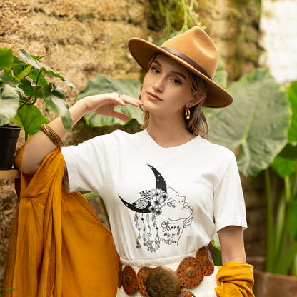"Strong as a Mother" Unisex Jersey T-Shirt, featuring a powerful graphic of a woman's profile emerging from a crescent moon, adorned with blooming flowers and delicate dangling charms, modeled by a Woman  wearing size M.