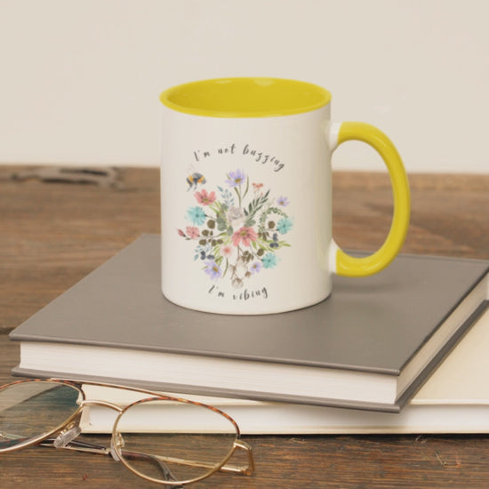  "I'm Not Buzzing, I'm Vibing" Bee & Wildflower Accent Coffee Mug, showcasing the charming bee and wildflower design on a white ceramic mug. Available in 11oz and 15oz sizes.