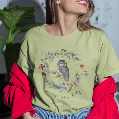 "Spring Vibes Only" Unisex Ultra Cotton Tee, featuring a charming watercolor illustration of a wise-looking owl perched within a circular wreath of spring flowers and foliage, with the text "Spring Vibes Only" in a playful script below, modeled by a woman, wearing size M. Color Pistachio 